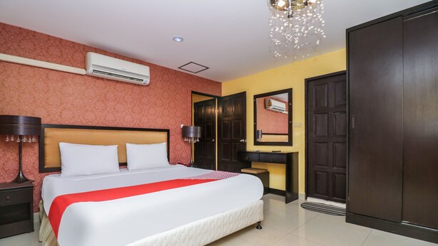 A hotel room with a large bed, a bedside table with a lamp, an air conditioning unit, a wardrobe, and a mirror. - OYO 131 Griebs Inn (Pattaya)