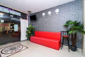 A reception area with a red sofa, a TV mounted on the wall, and a potted plant. - OYO 131 Griebs Inn (Pattaya)