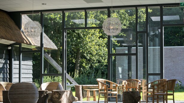 A spacious indoor area with large windows, wooden furniture, and a thatched roof structure. - Buitengoed Fredeshiem (De Bult)