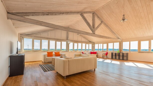A spacious living room with a high ceiling, wooden beams, large windows, a sofa, a coffee table, and a TV. - Agriturismo Masseria Cannella (Poggio Imperiale)