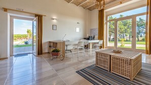 A spacious room with a large sliding glass door leading to a garden, a wooden desk with a computer, white chairs, and a small table with a basket. - Agriturismo Masseria Cannella (Poggio Imperiale)