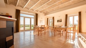 A spacious dining area with a large table and chairs, a fireplace, and large windows offering a view of the outdoors. - Agriturismo Masseria Cannella (Poggio Imperiale)