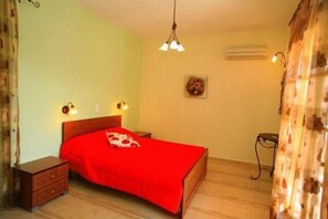 A bedroom with a wooden bed, a nightstand, a hanging light fixture, and a wall-mounted air conditioner. - Emily's Apartments (Corfu)