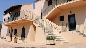 A two-story building with a balcony on the upper floor, a staircase leading to the upper level, and potted plants in front. - Emily's Apartments (Corfu)