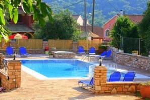 A swimming pool with blue lounge chairs and stone walls. - Emily's Apartments (Corfu)