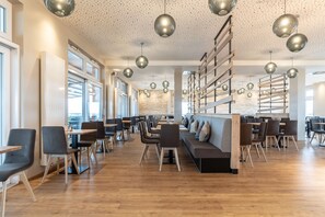 Un restaurante moderno con suelo de madera, asientos negros y grises, e iluminación colgante.
