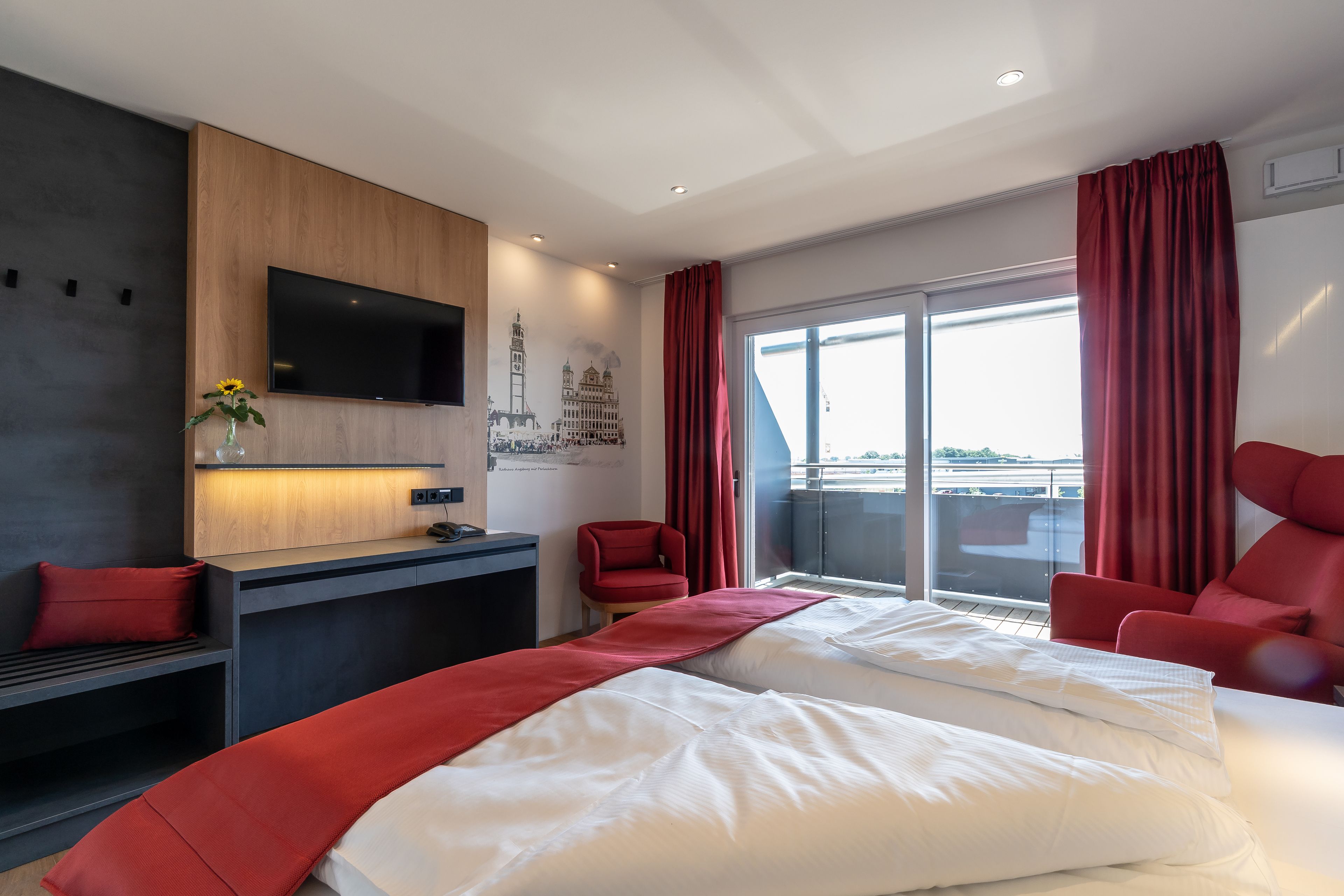 A modern hotel room with a large bed, a desk, a TV, and a balcony with red curtains.