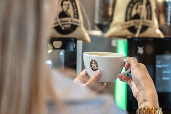 Una persona sosteniendo una taza con un logotipo, en un entorno con bolsas colgadas al fondo.