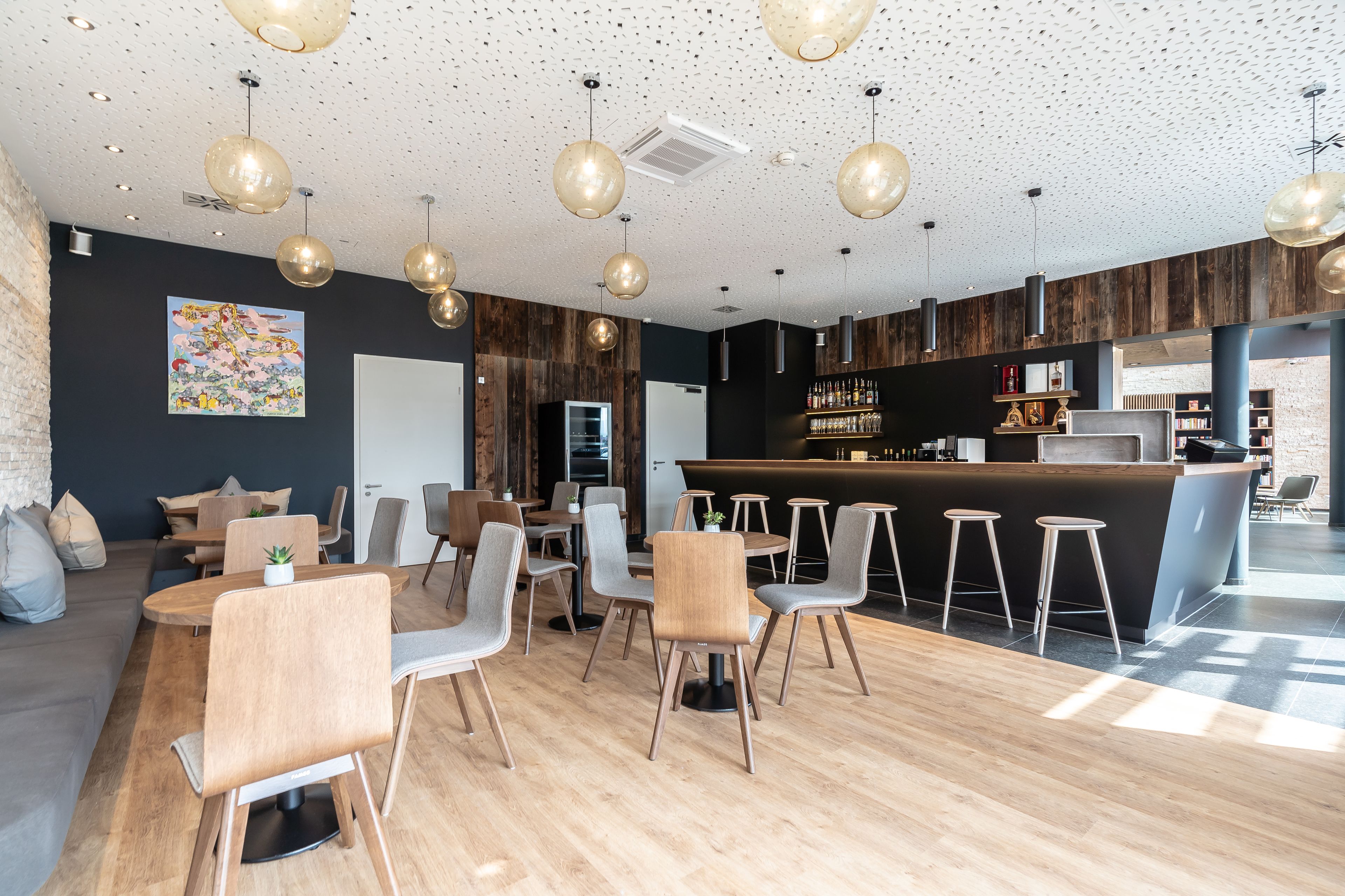 Un espace repas moderne avec des tables et des chaises en bois, des luminaires suspendus et un coin bar avec des tabourets.
