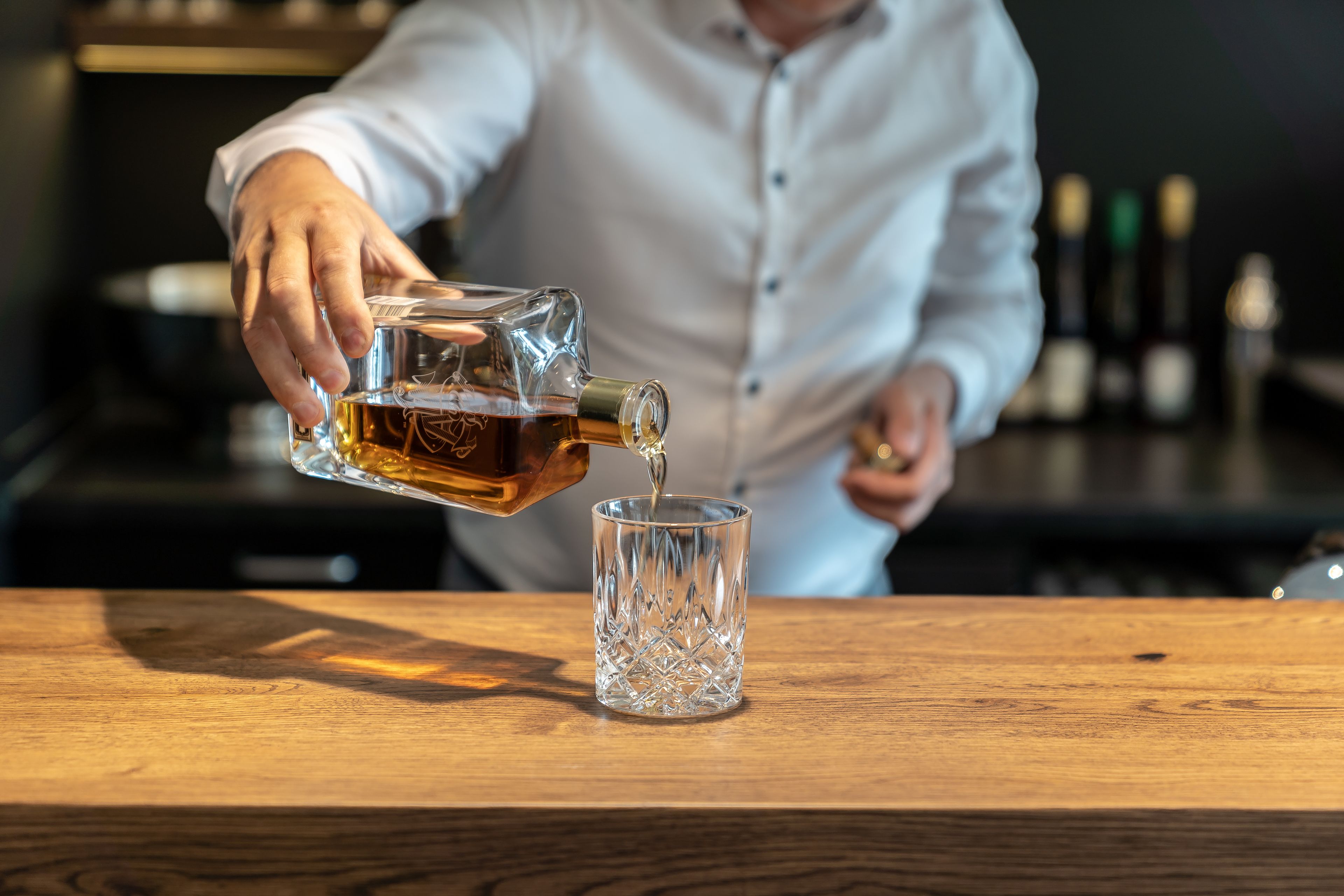 A person pouring a drink into a glass on a wooden table.