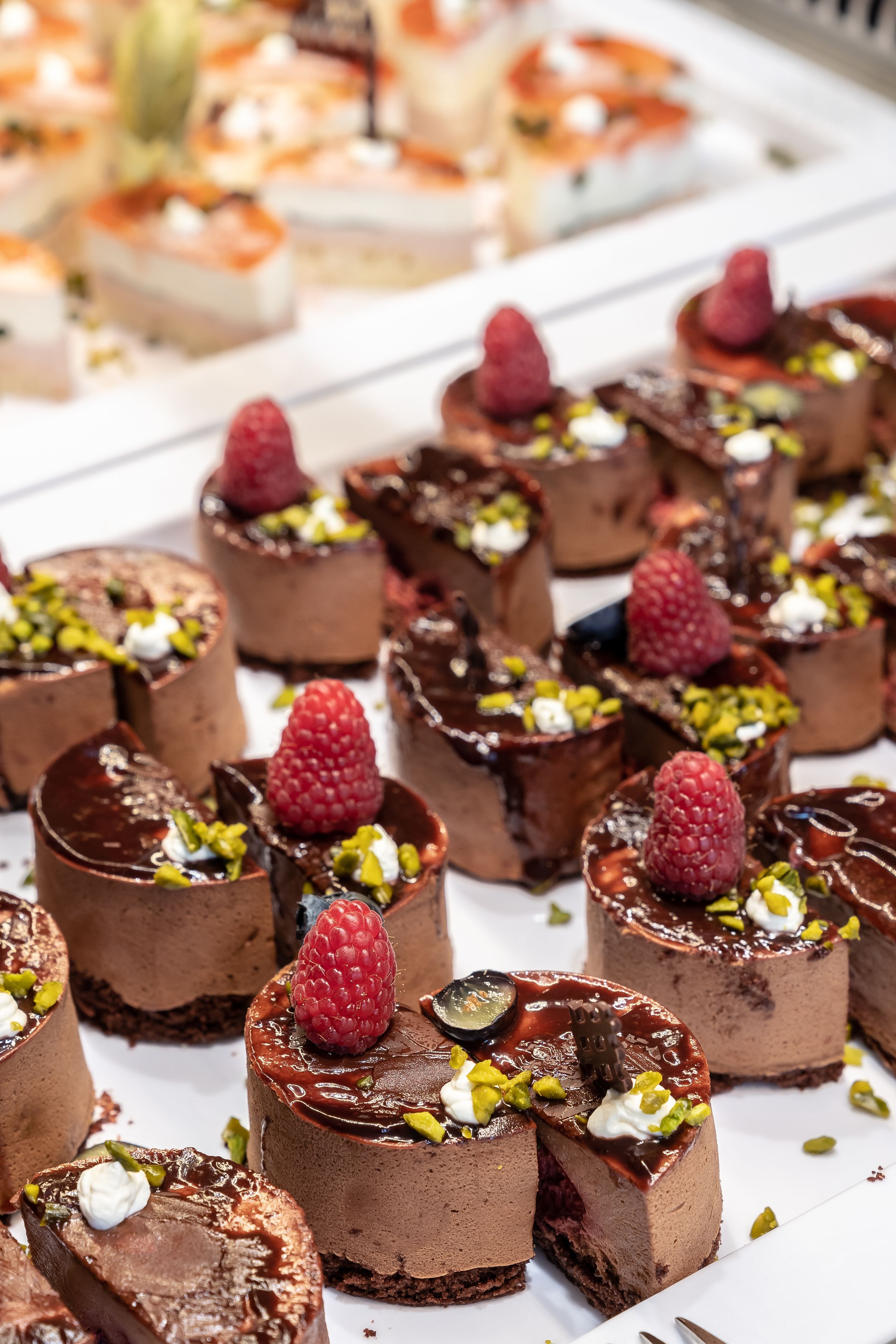 A variety of desserts, including chocolate mousse cups topped with raspberries and pistachios.