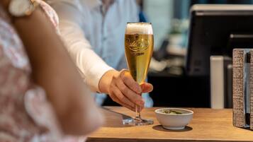En person holder et glas øl ved et bord med en skål mad og en bog.