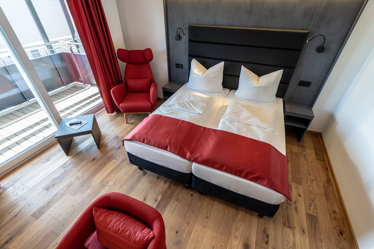 Une chambre d’hôtel moderne avec un grand lit, un fauteuil rouge et une vue sur le balcon.