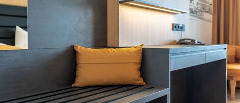 Habitación de hotel moderna con un banco, un escritorio, un espejo y una planta.