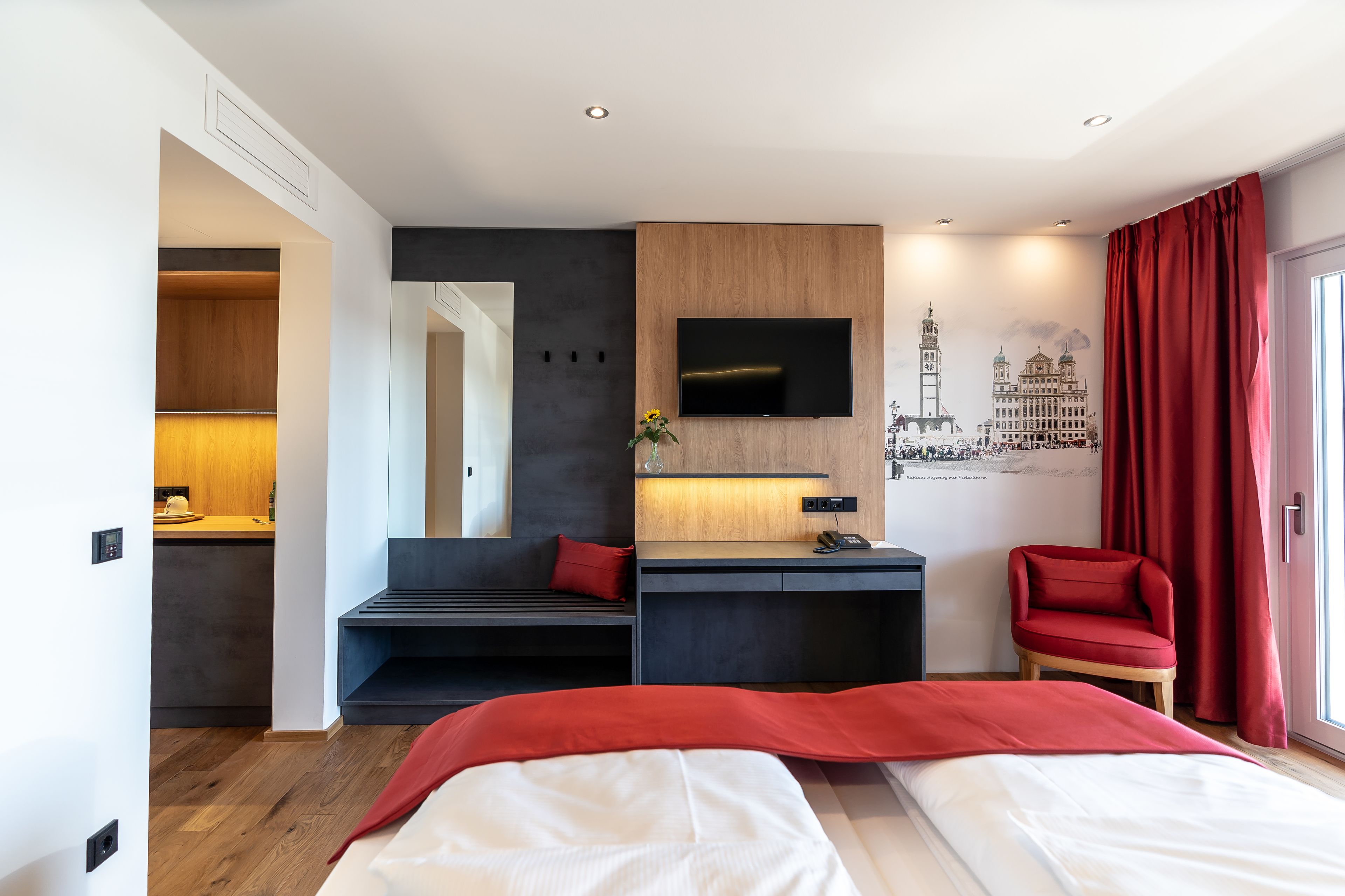 Una habitación de hotel moderna con una cama, un escritorio, un televisor y una silla roja.