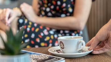 Una taza blanca con un logotipo sobre un plato, una pequeña planta verde y un menú sobre una mesa de madera.