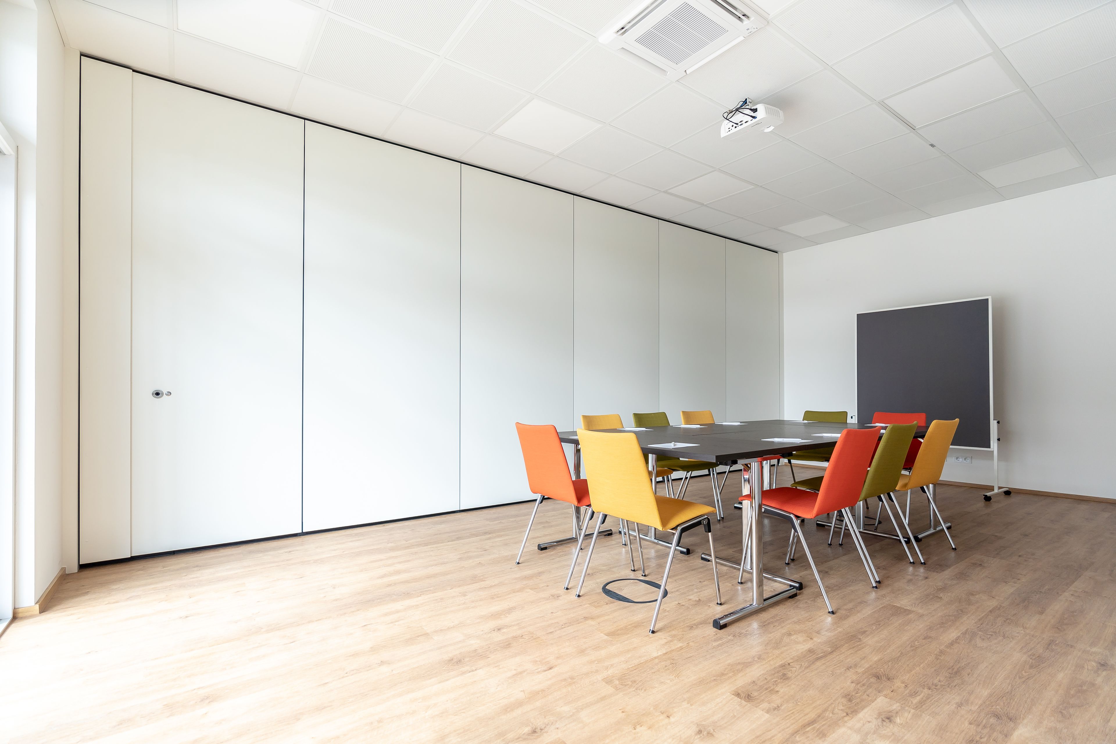 A conference room with a large table, colorful chairs, a whiteboard, and a wooden floor.