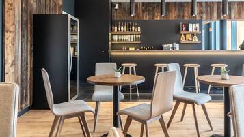 A modern bar area with round tables and chairs, wooden flooring, and a bar counter with shelves of bottles and glasses.