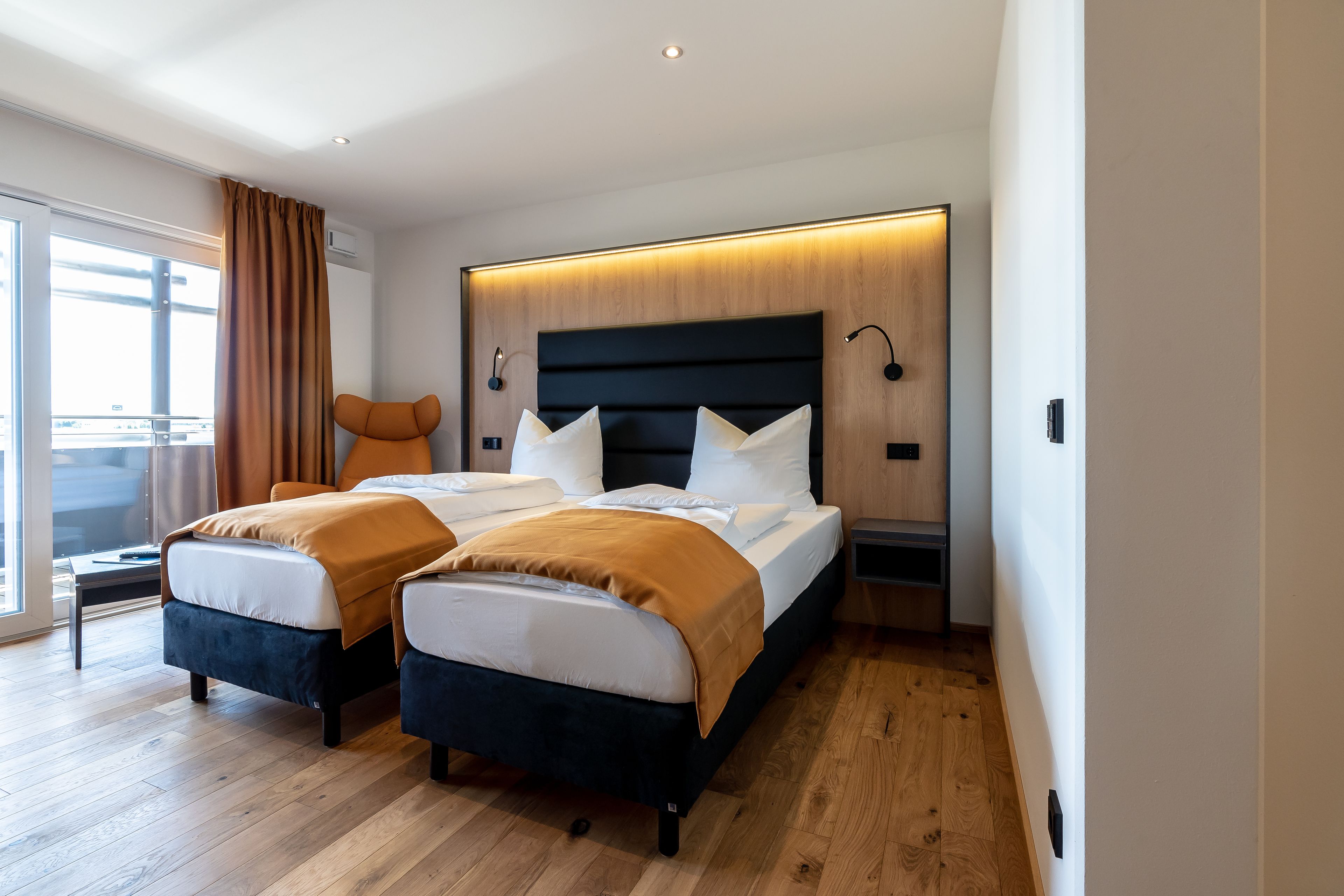 A modern hotel room with a large bed, two bedside tables, a nightstand, and a view of the outdoors.