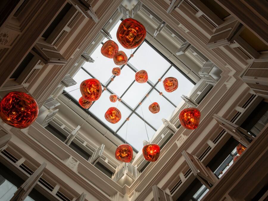 A high ceiling with multiple windows and hanging red spherical light fixtures.