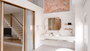 Ein modernes Badezimmer mit einer freistehenden Badewanne, einem großen Spiegel und einer Wand mit Backsteinverkleidung.