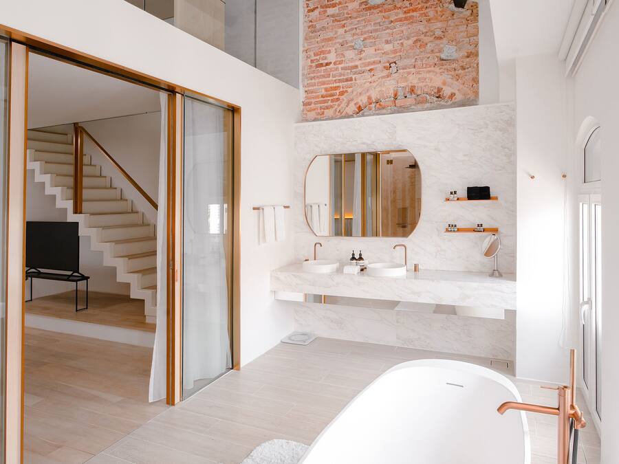 A modern bathroom with a freestanding bathtub, a large mirror, and a brick accent wall.
