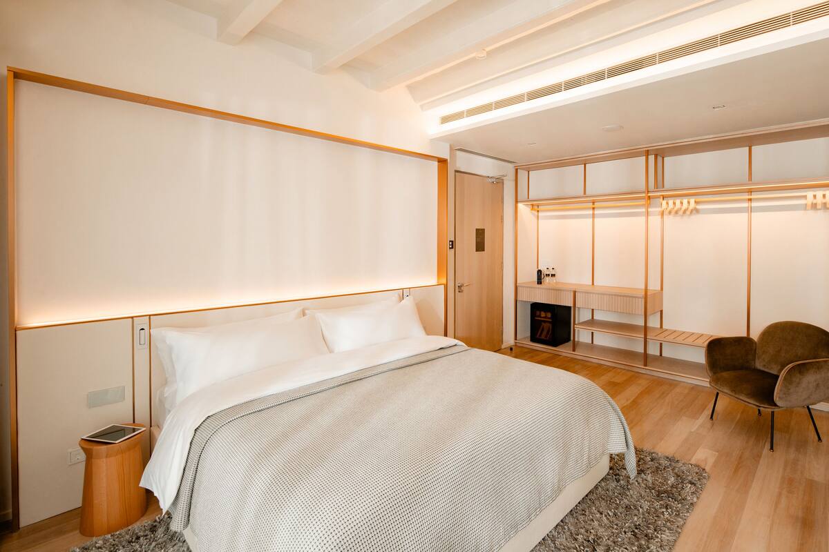 A modern bedroom with a large bed, a walk-in closet, and a seating area.