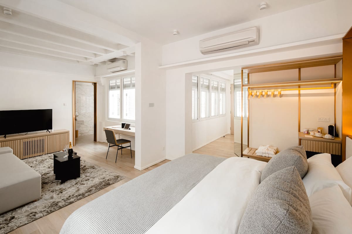 A modern hotel room with a large bed, a desk, a TV, and a walk-in closet.