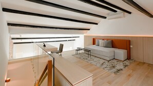 Ein modernes Wohnzimmer mit einer Couch, einem Couchtisch und einem Schreibtisch mit Stuhl. Eine Treppe mit Geländer führt auf eine erhöhte Ebene.