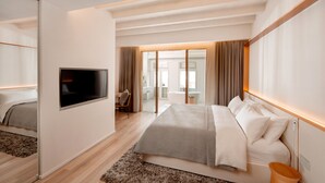 Ein modernes Hotelzimmer mit einem großen Bett, einem flachbildfernseher an der Wand, Holzboden und Blick ins Freie durch eine Schiebetür.