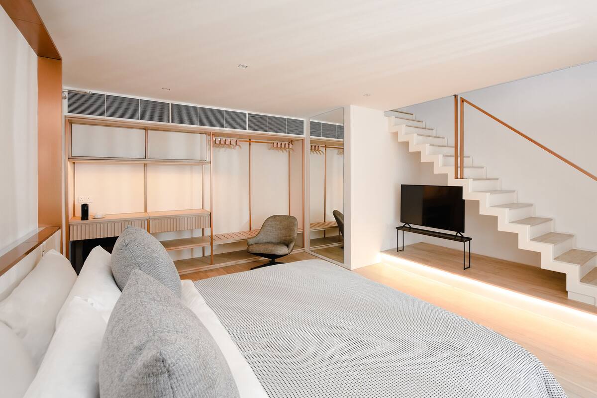 A modern bedroom with a bed, a TV, a chair, a closet, and a staircase.