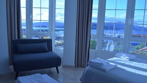 A hotel room with a bed, a sofa, and a view of a marina and mountains. - Pensión O Noso (Porto do Son)