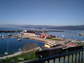 A marina with boats, a building with a red roof, and a clear view of the water and distant mountains. - Pensión O Noso (Porto do Son)