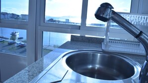 A kitchen with a stainless steel sink and a window overlooking a cityscape. - Pensión O Noso (Porto do Son)