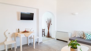 Un salon moderne avec un téléviseur à écran plat fixé au mur, un coin repas avec une table et des chaises, un canapé agrémenté de coussins à motifs et une plante en pot posée sur une table basse.