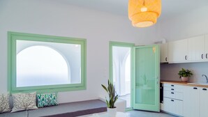 Une cuisine moderne avec des meubles blancs, une fenêtre à cadre vert, une table ronde sur laquelle repose un livre et une plante en pot.