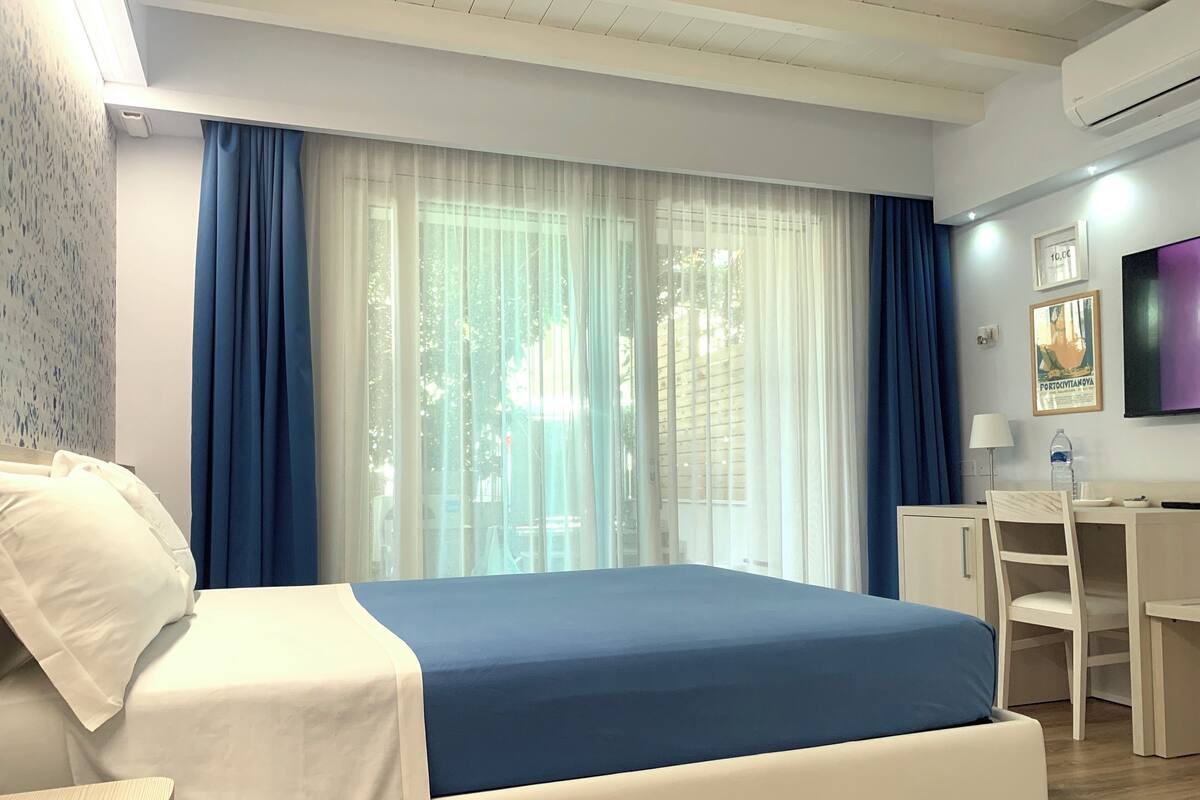 Ein Hotelzimmer mit Bett, Schreibtisch, Sessel, Fernseher und einem Fenster mit Vorhängen.