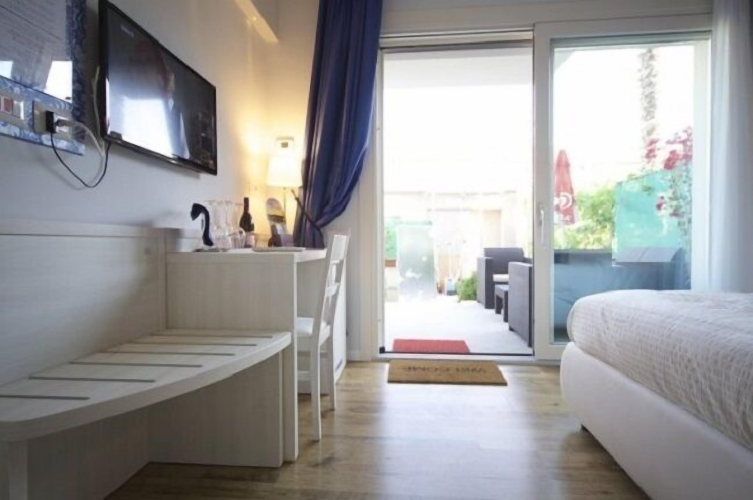 Una habitación de hotel moderna con una cama, un banco empotrado, un televisor y una puerta de vidrio corredera que da a un espacio exterior.
