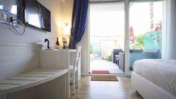 Una habitación de hotel moderna con una cama, un banco empotrado, un televisor y una puerta de vidrio corredera que da a un espacio exterior.