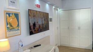 Een hotelkamer met een bed, een bureau met een lamp, een waterfles, een afstandsbediening en een lijst aan de muur.