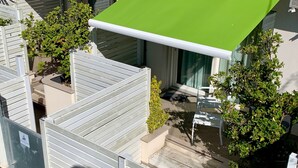 Een modern balkon buiten met een groene luifel, witte leuningen en potplanten.
