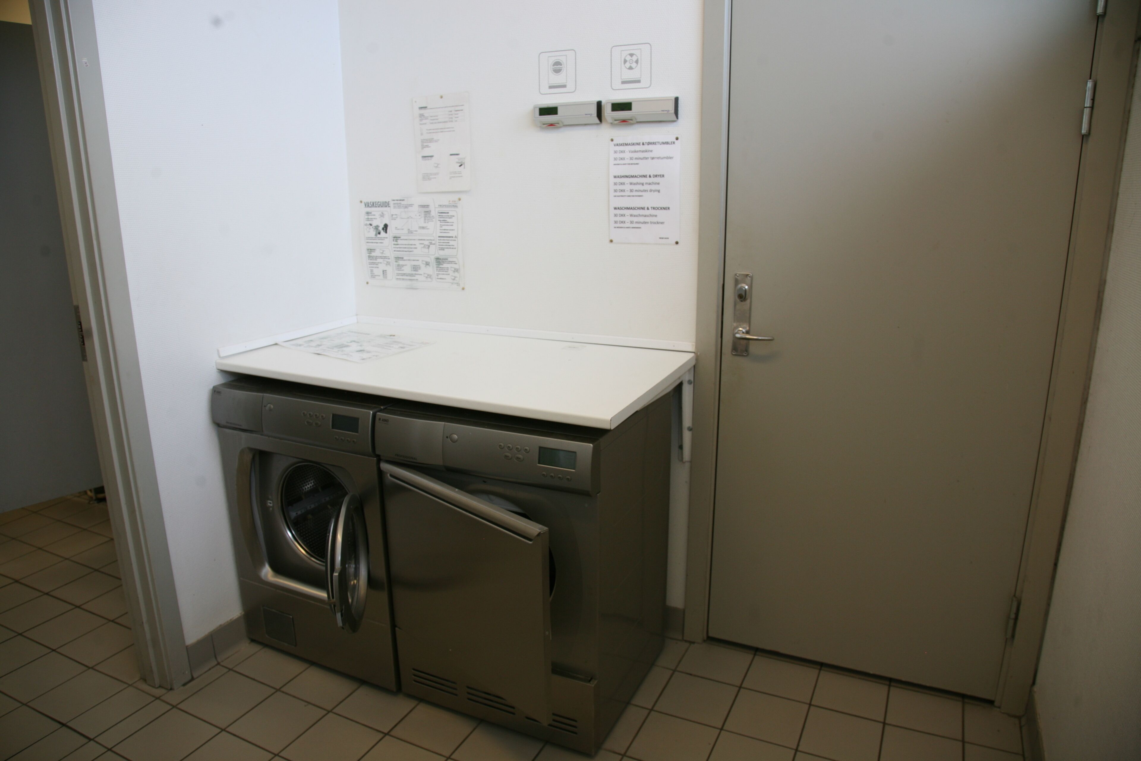 Ein kleiner Waschraum mit Waschmaschine und Trockner, einer weißen Arbeitsplatte und einer abschließbaren Tür.