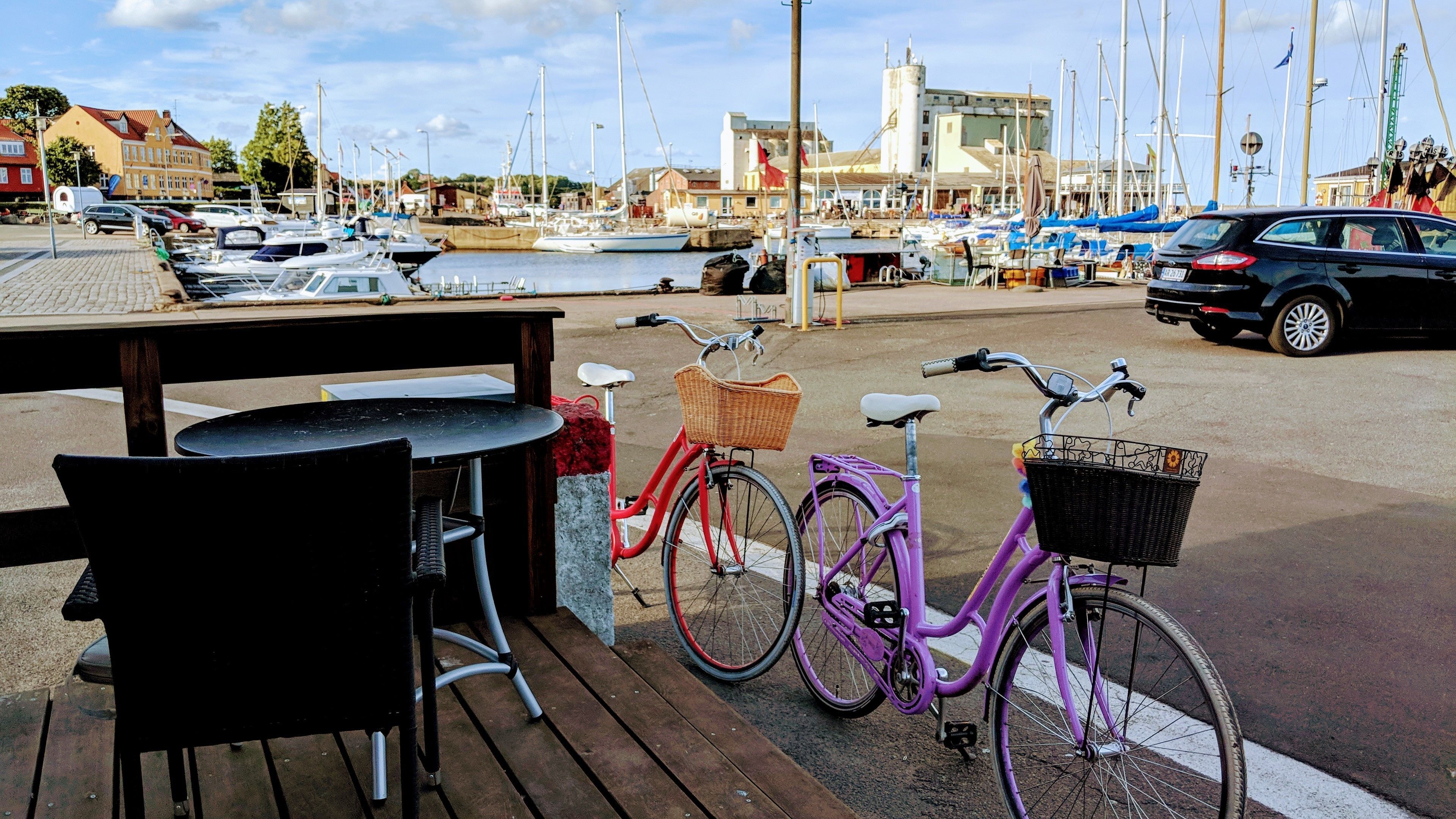 Puerto deportivo con barcos, un banco de madera y una bicicleta morada con cesta.