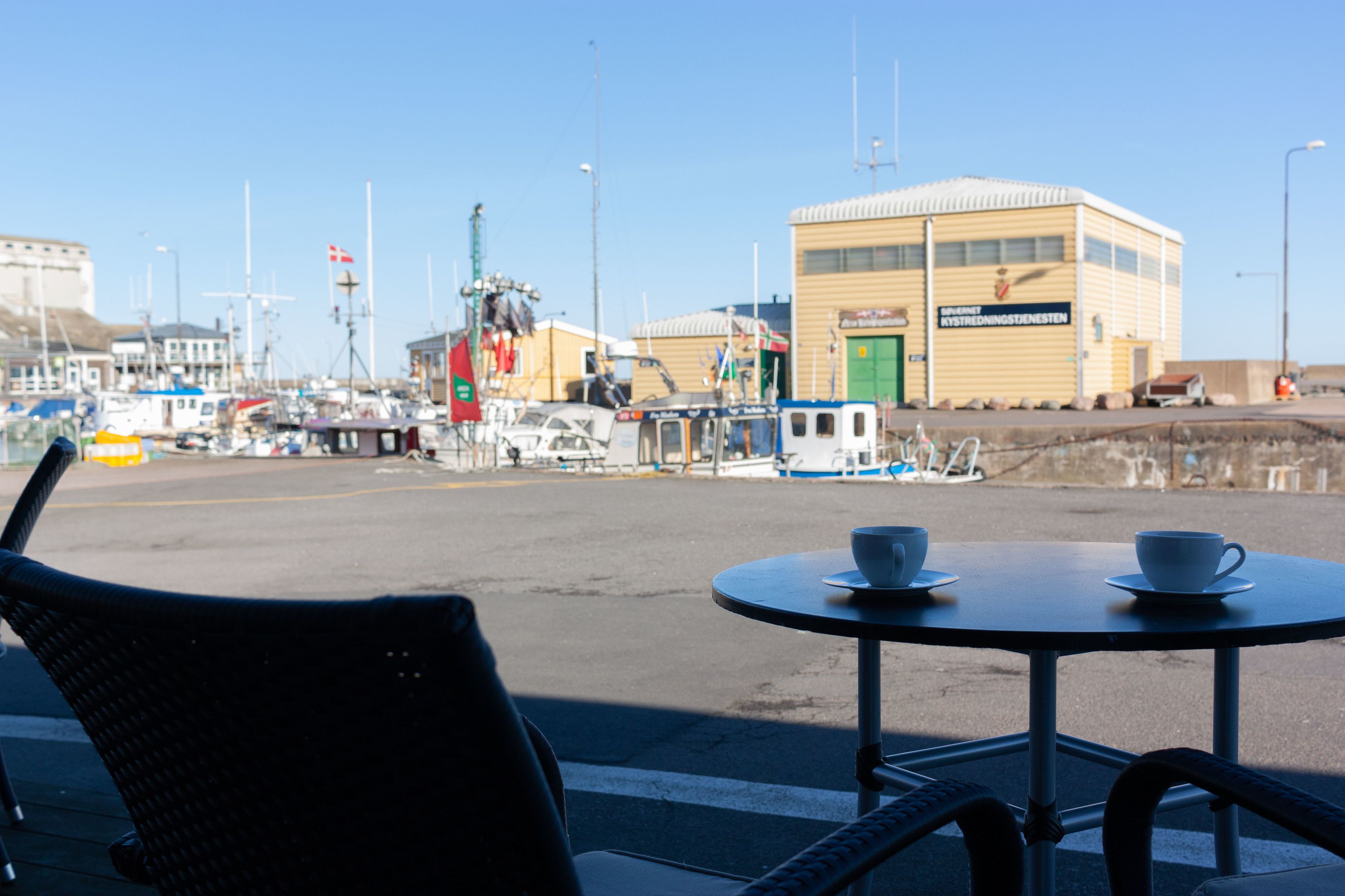 A view of a harbor with boats, a building with a green door, and a table with cups.