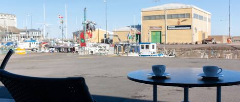 A view of a harbor with boats, a building with a green door, and a table with cups.