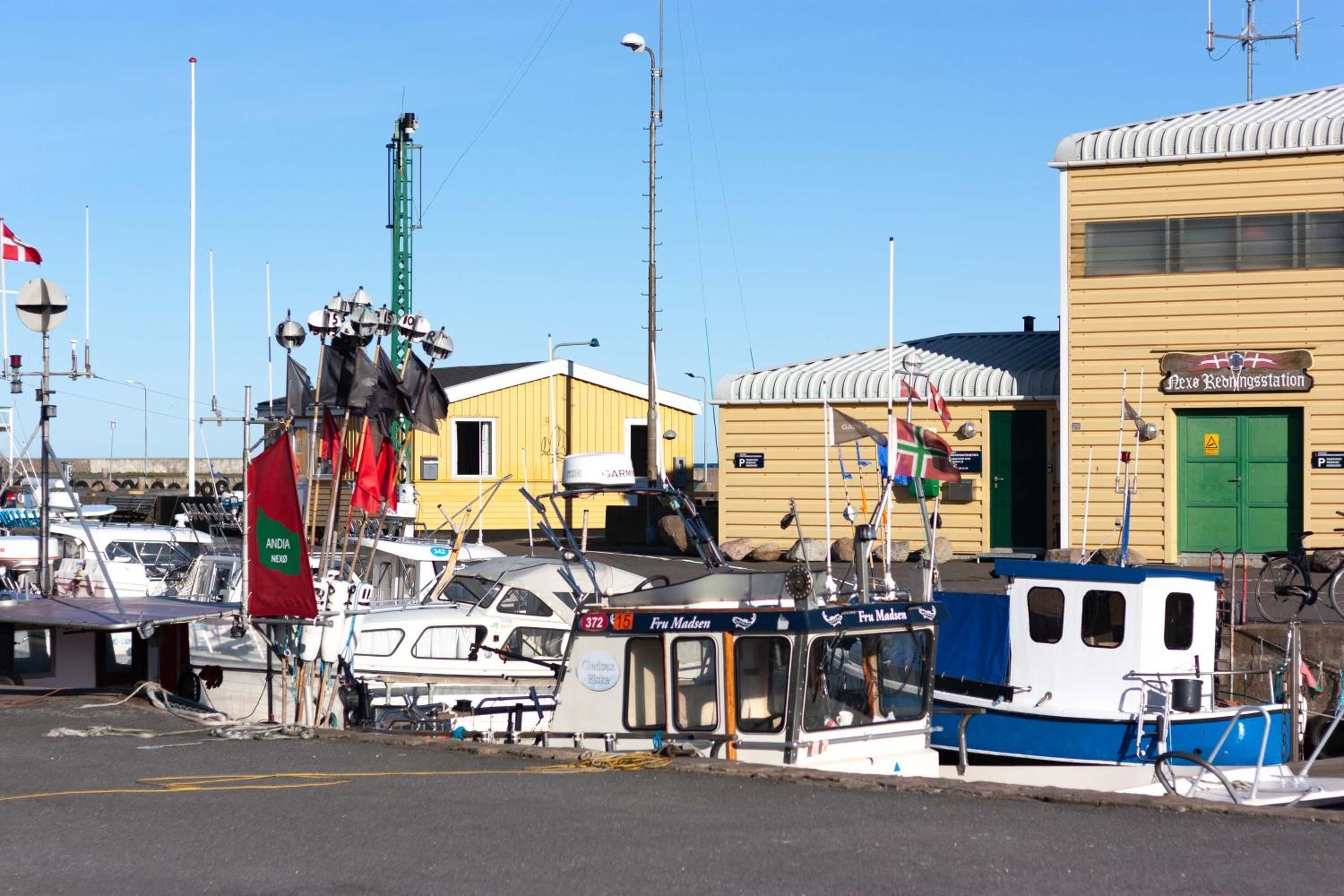 A marina with boats docked, a yellow building labeled "Rexe Redningsstation," and a green door.