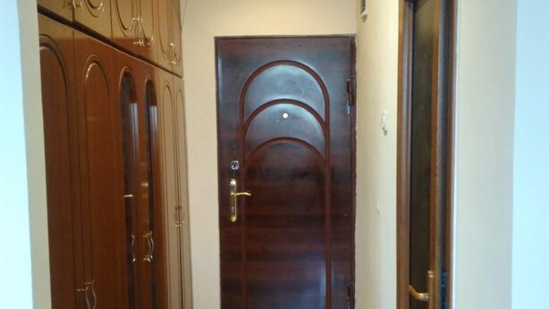 Ein Korridor mit einem gemusterten Boden, einer Holztür mit Metallbeschlag und einem Schrank mit Spiegelüren.
