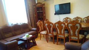 Ein Wohnzimmer mit braunem Sofa, passenden Sesseln, einem Holztisch und einem an der Wand montierten Fernseher.