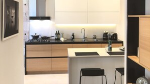Een moderne keuken met een centraal eiland, hangende lampen en uitzicht op de eetruimte.