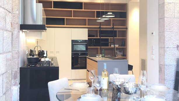 Een moderne eethoek met een glazen tafel, witte stoelen en een keuken op de achtergrond.
